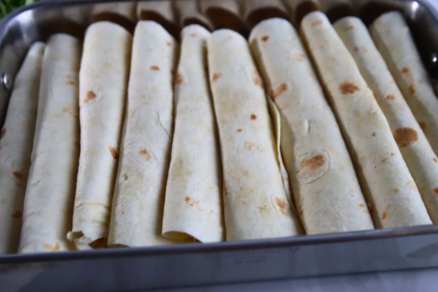 2025-04-26-18.01.36-2-1536x1024.webp Eight rolled chicken enchiladas arranged in a rectangular baking pan.