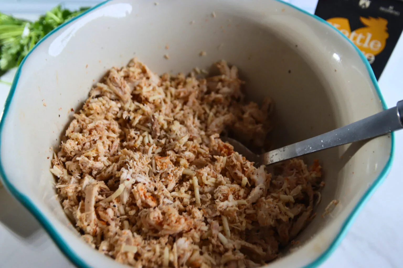 2025-04-26-18.01.39-1536x1024.webp Shredded chicken mixed with Monterey Jack cheese and Dia de la Fajita seasoning in a bowl.